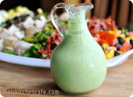 green salad dressing in front of a white plate of salad