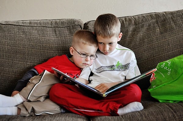 Two little boys reading on a couch together.