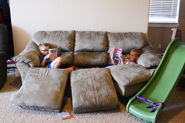 Two little boys reading on a couch with no cushions.
