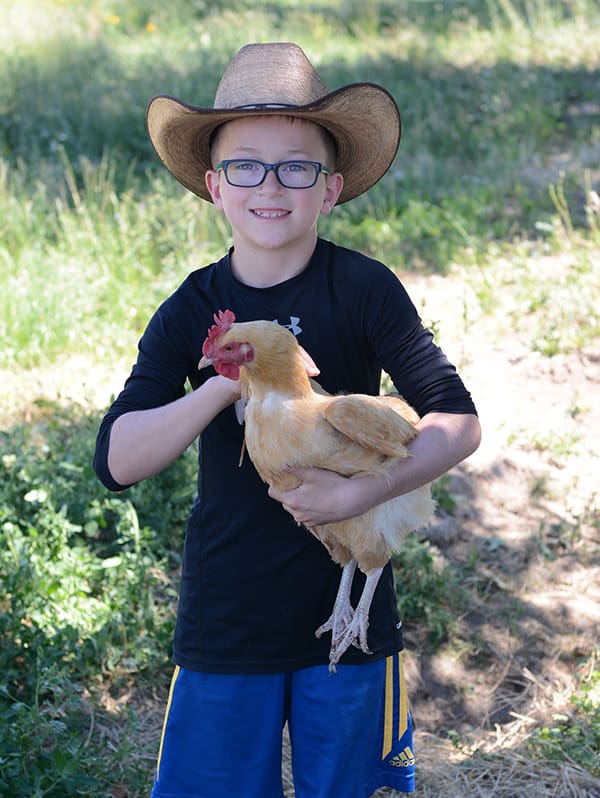 A little boy in a cowboy hat holding a chicken.