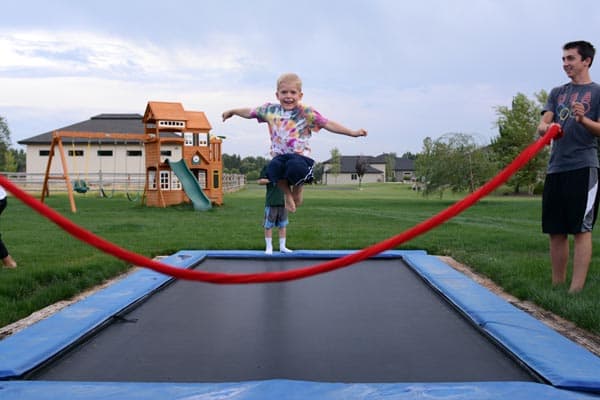 A little boy jumping over a red rope on a tramp.