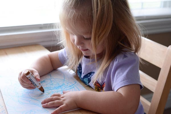 A little girl sitting at a table drawing a picture.