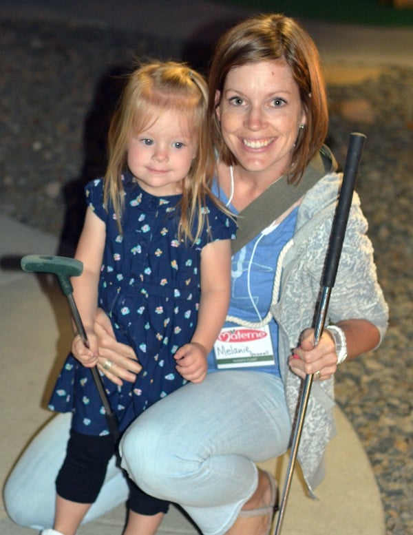 A Mom and daughter holding putt putt golf clubs. 