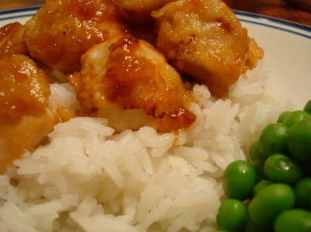 Sticky honey glazed chicken, white rice, and green peas on a plate.