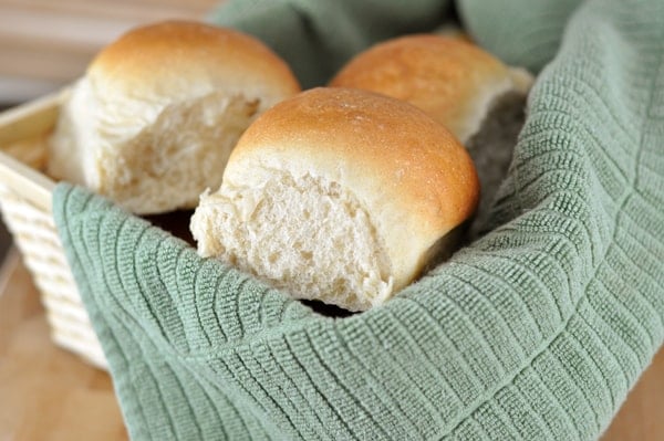 Three white french bread rolls in a basket with a green towel.