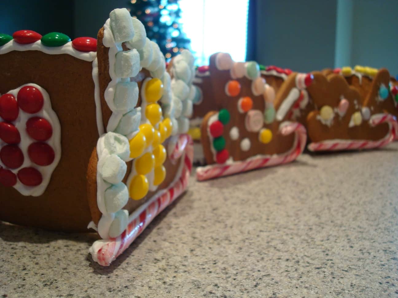 Three gingerbread sleds decorated with frosting and candy in a line on a countertop.