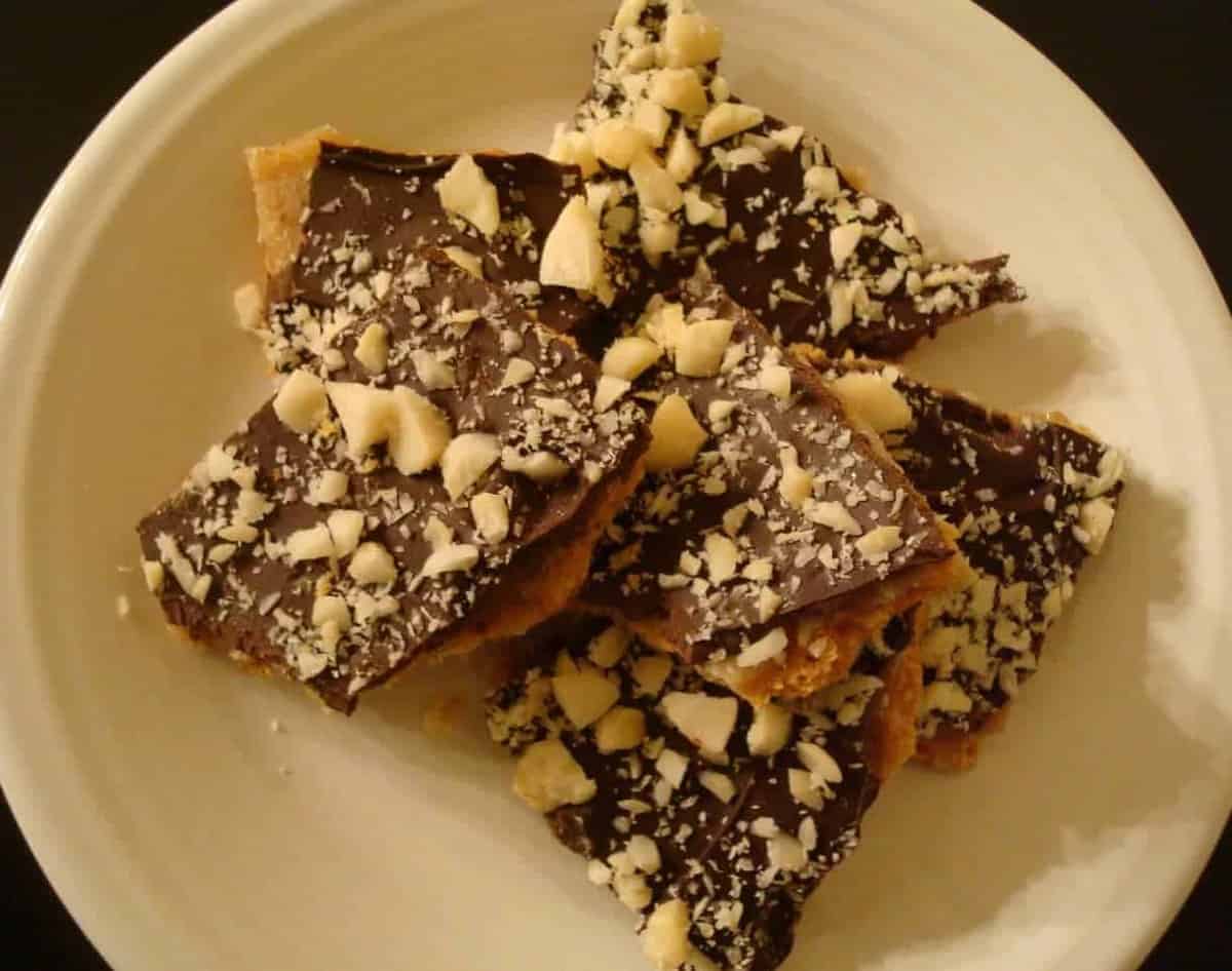 Chunks of chocolate caramel toffee topped with crushed macadamia nuts on a white plate.