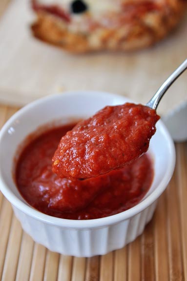 A spoonful of pizza sauce being taken out of a ramekin of pizza sauce.