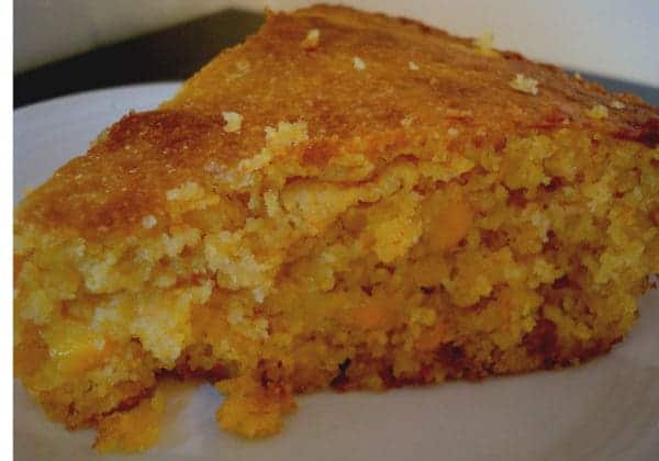 A thick triangle-shaped piece of cornbread on a white plate.