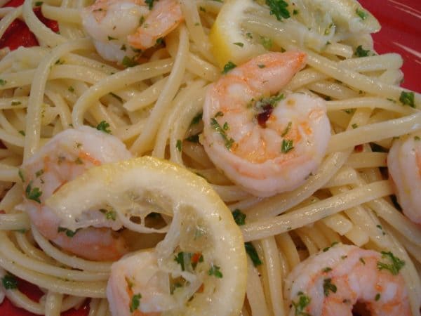 A plate of linguine, shrimp scampi and a lemon slice.