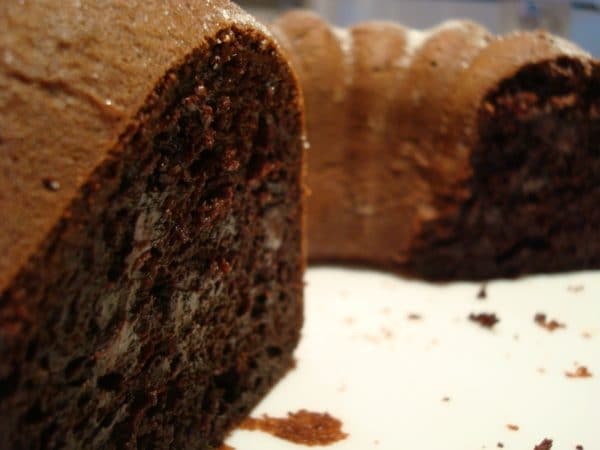 A chocolate bundt cake with a slice taken out on a white plate.