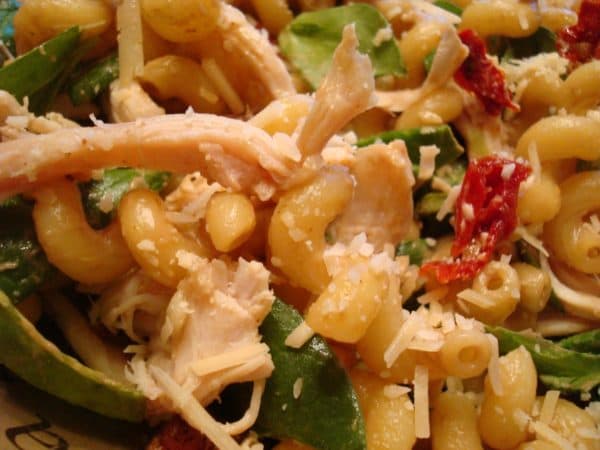 Pasta salad with macaroni noodles and spinach and tomatoes mixed in.
