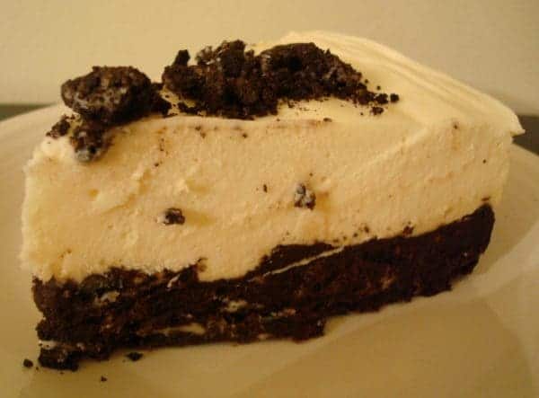 A piece of white chocolate torte with a mousse filling and an oreo crust on a white plate.