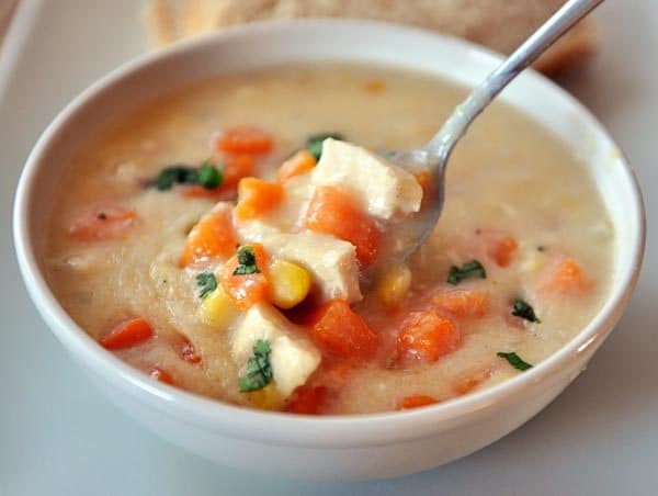 a white bowl of chowder with chicken chunks, sweet potato, and a spoon in it