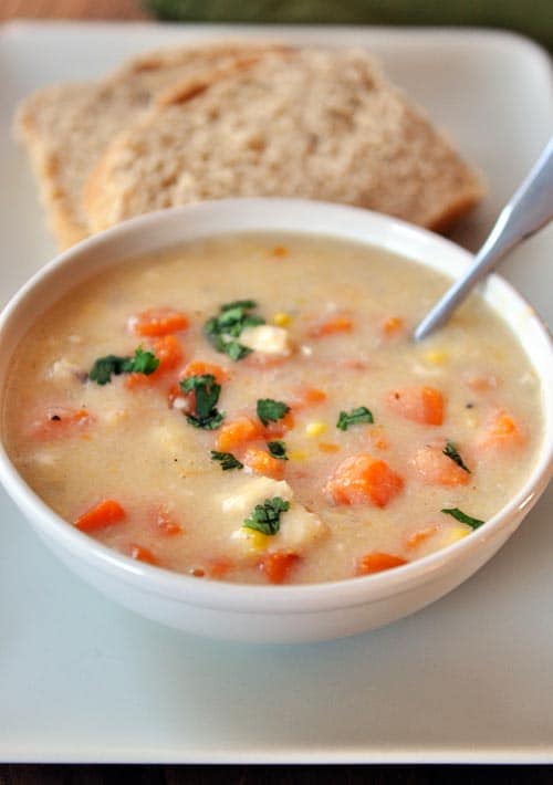 A white bowl of chowder with chunks of chicken, sweet potatoes, and corn.