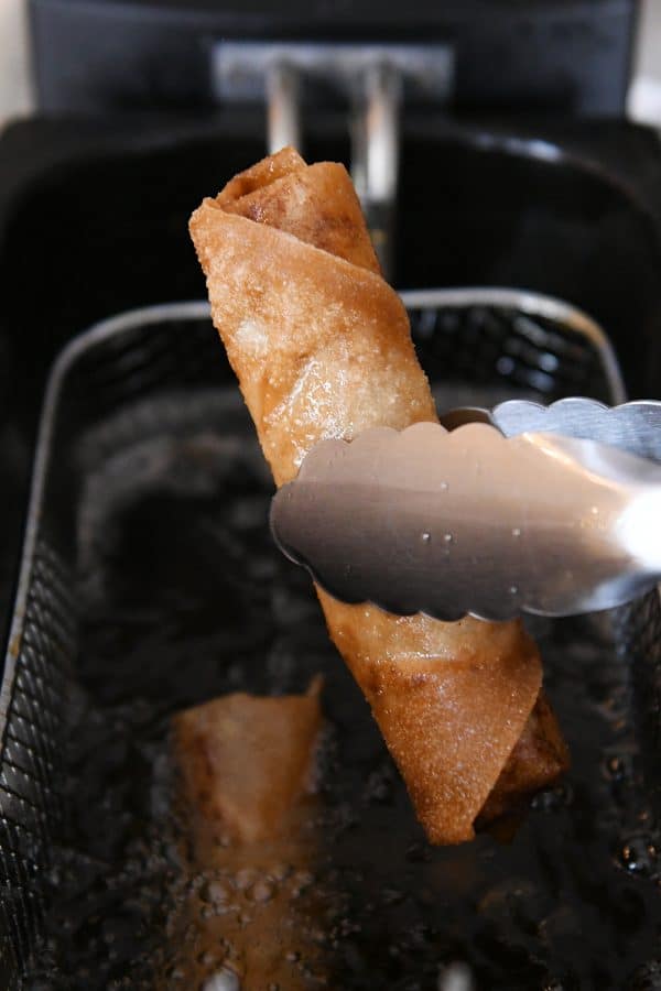 an egg roll held with tongs being pulled out of a fryer