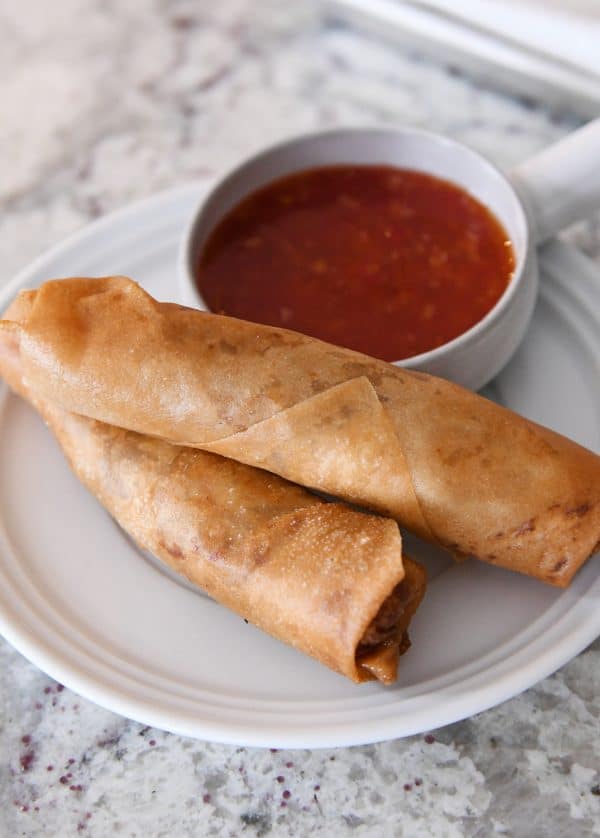 Two egg rolls and a bowl of dipping sauce on a white plate.