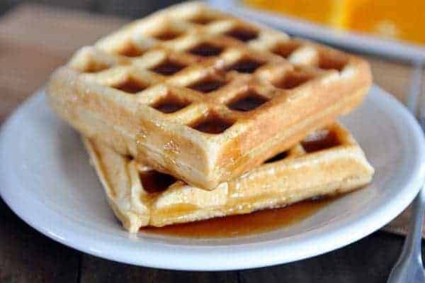 Two waffle squares stacked on top of a white plate and covered in syrup.