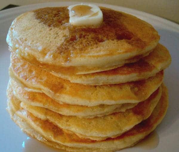 Stack of pancakes topped with a pat of butter and syrup on a white plate.