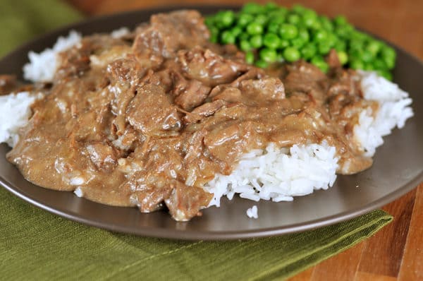 beef stroganoff over a bed of white rice and a scoop of green peas on the side