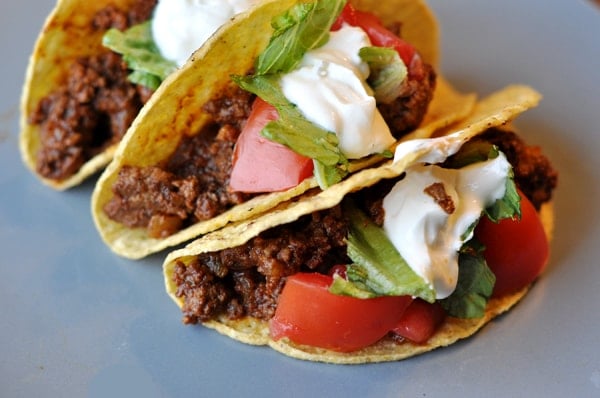 three filled ground beef tacos topped with sour cream lettuce, and tomatoes