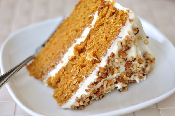 A slice of carrot cake with two layers, white frosting in the middle, and chopped nuts on top on a plate.