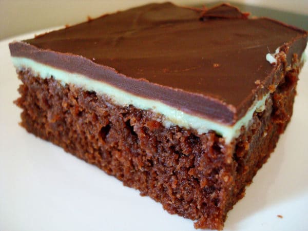 Brownie with mint layer and chocolate frosting on a white plate.