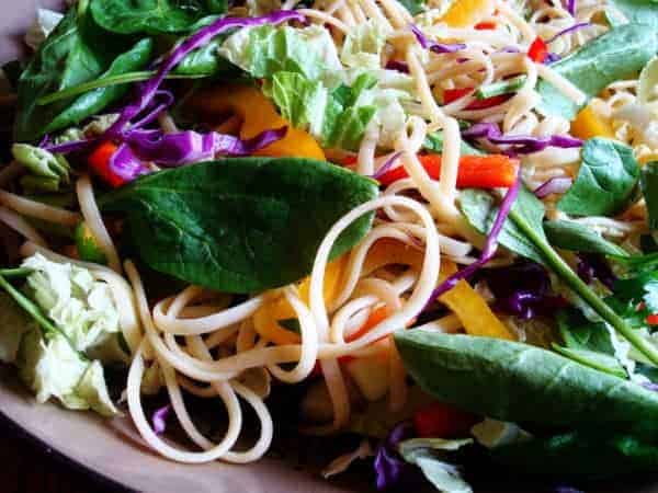 Noodles, peppers, and spinach in a white bowl.