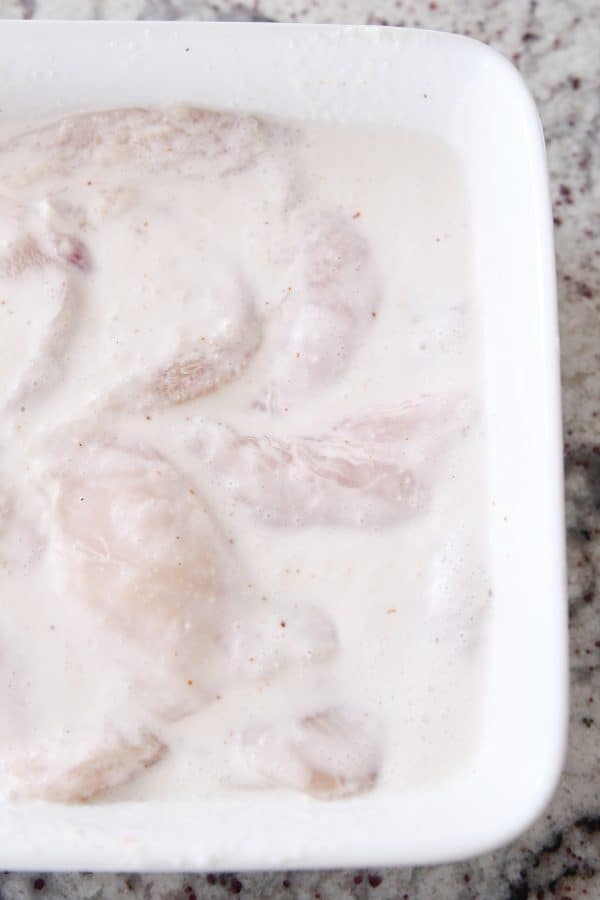 A white casserole dish of chicken marinating. 