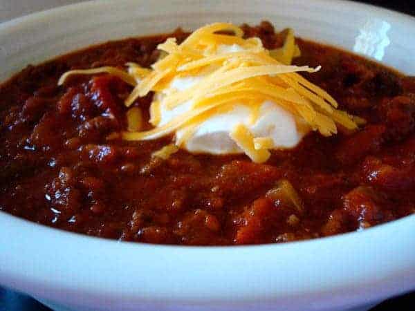 White bowl with chili topped with sour cream and cheese.