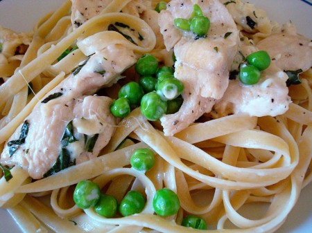 Fettuccine noodles topped with chicken and peas.
