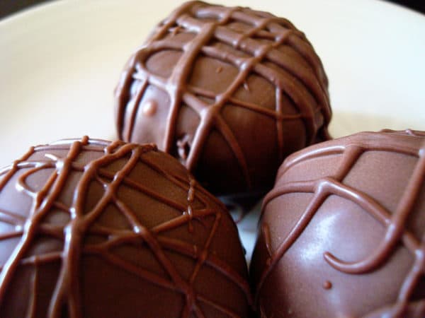 three chocolate covered truffles on a white plate