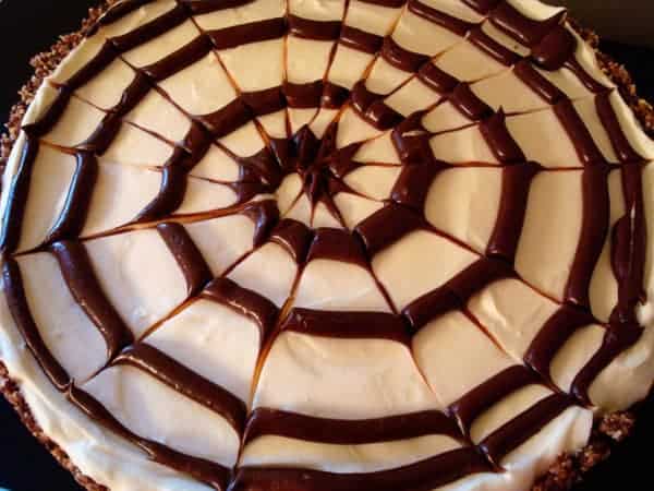 Top view of a cheesecake with a spiral chocolate spiderweb on top.