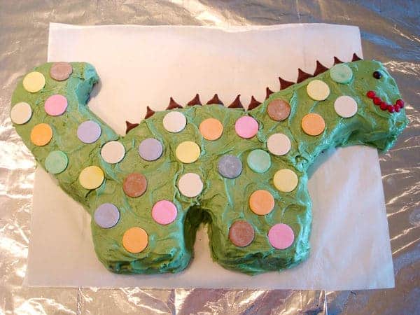Frosted dinosaur cake with chocolate spikes and colored spots.