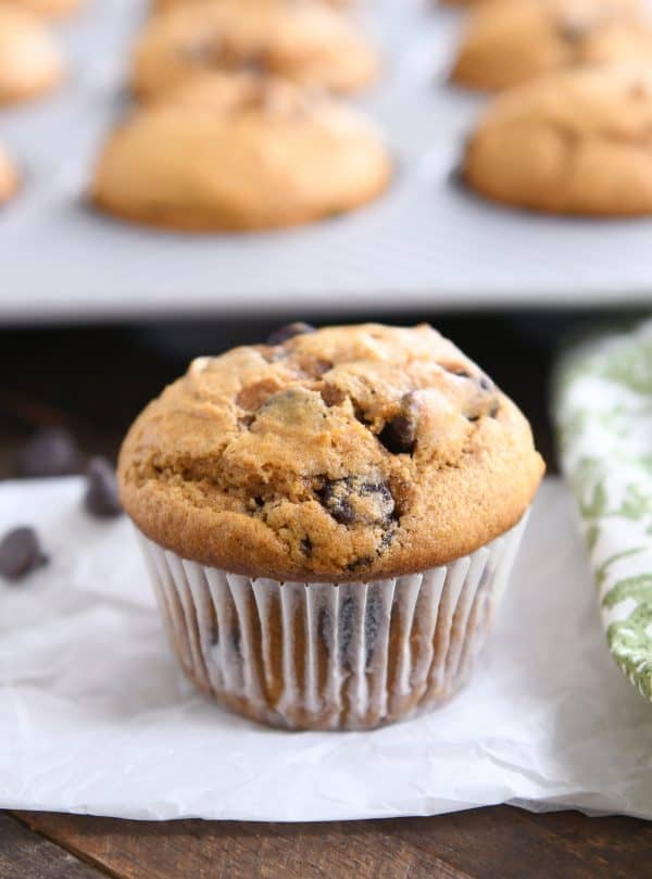 Pumpkin chocolate chip muffin in liner on white napkin.