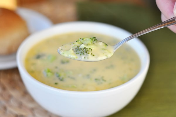 White bowl of broccoli cheese soup with spoon taking a bite out.