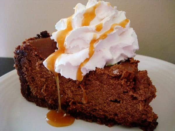 Slice of chocolate cheesecake topped with whipped cream and caramel drizzle.