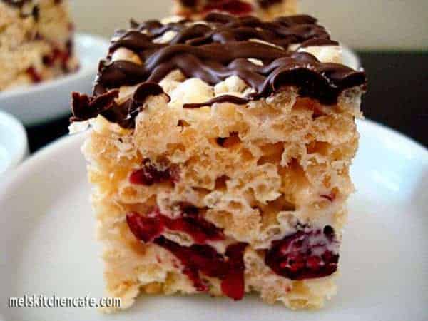 Rice krispie treat with chocolate drizzle and cranberries on a white plate.
