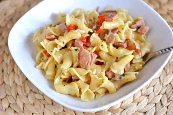 Pasta with ham and peppers in a white bowl.