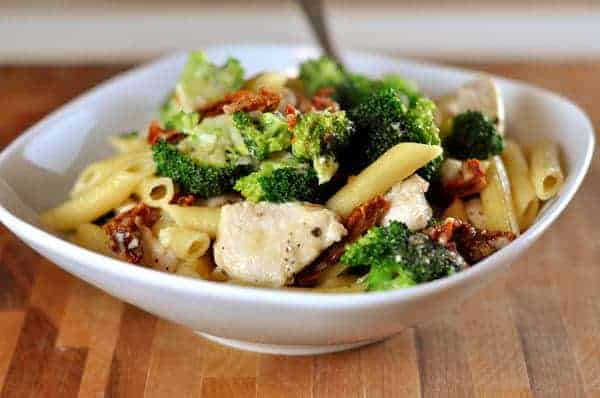 White bowl of pasta, chicken, broccoli, and sun-dried tomatoes.