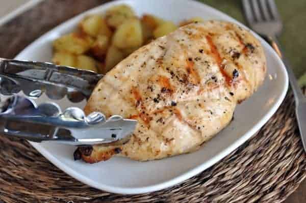 grilled chicken breast on white plate being lifted with tongs