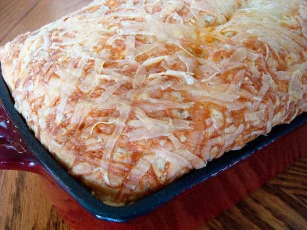 Cheese covered loaf of bread in a bread tin.