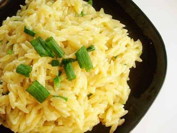 Black bowl with cooked orzo and chopped chives.