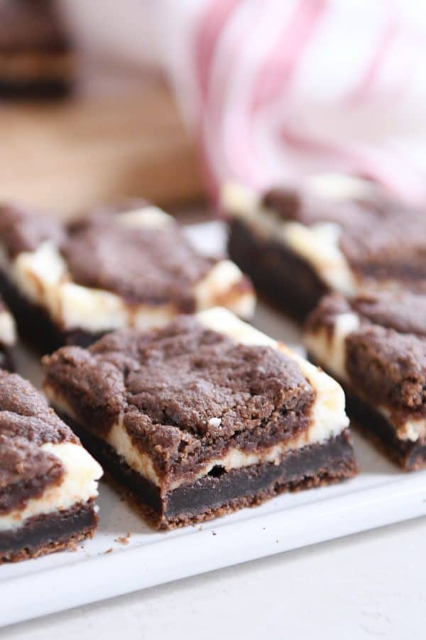 Cut squares of black and white cheesecake brownies on white platter.