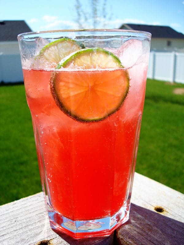 Glass filled with raspberry drink, lime, and ice.