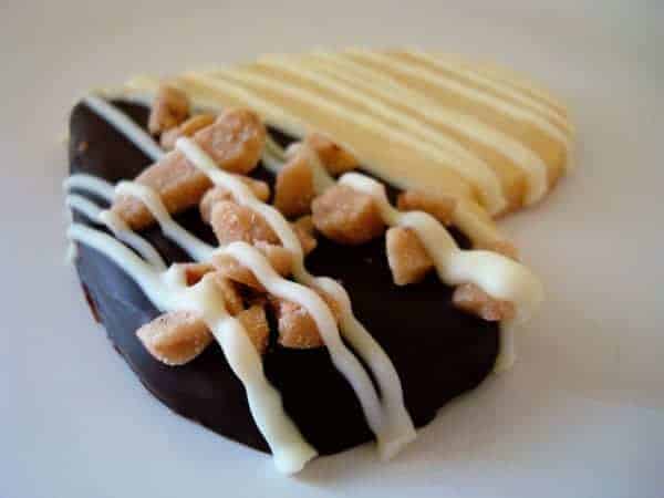 Heart shaped sugar cookie with half dipped in chocolate and bits of toffee.