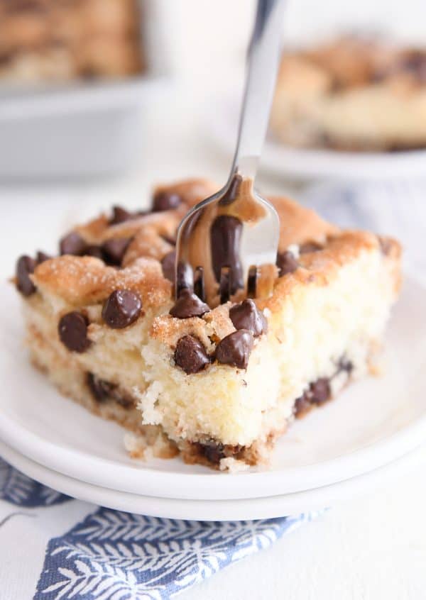 Fork taking bite out of chocolate chip cake on white plate.