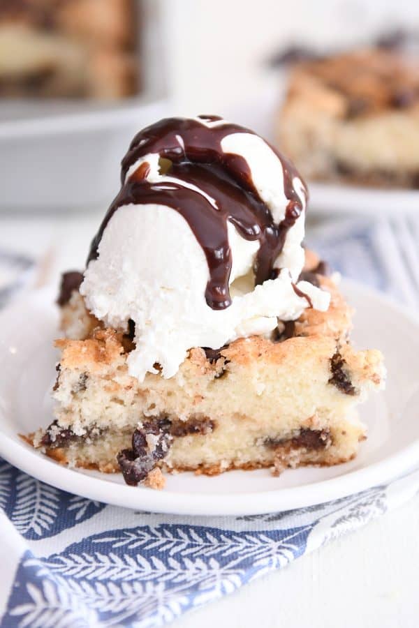 Piece of one bowl chocolate chip cake on white plate with ice cream and hot fudge sauce.
