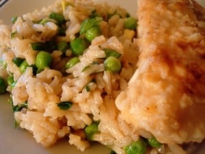 Rice and peas and a piece of chicken on a white plate.