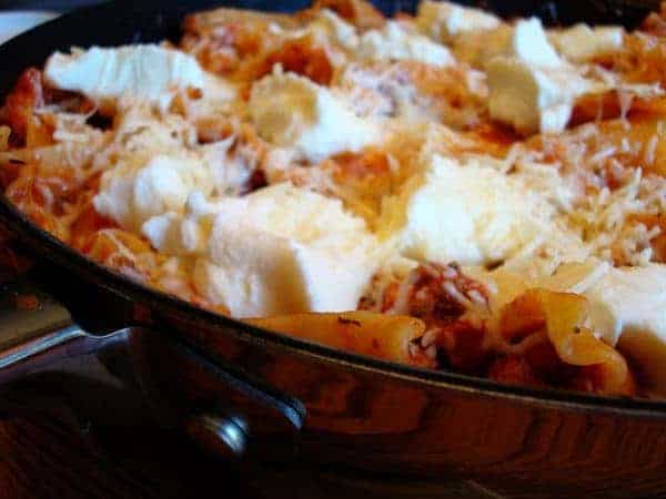 Skillet full of cooked lasagna and melted cheese.